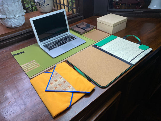 A desk surface with a laptop on a deskmat, a planner laid open, and a big yellow envelope on the side.