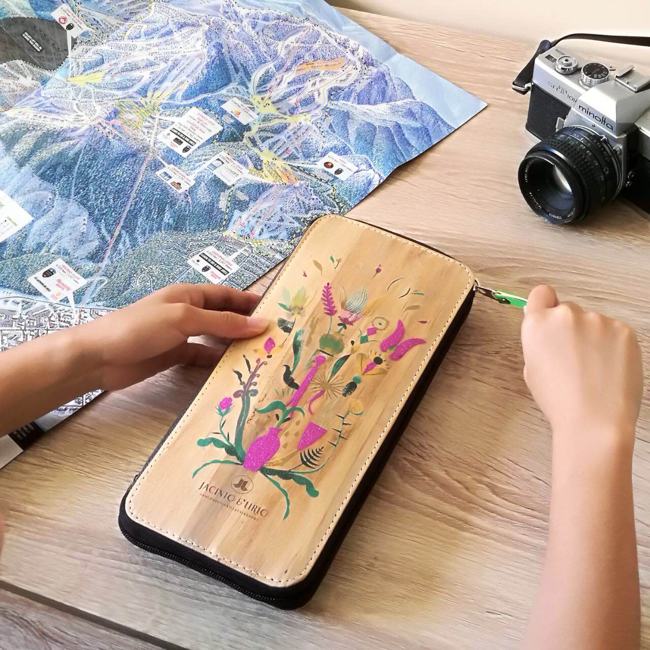 A vegan leather zipped wallet with a vibrant purple and green abstract design on its cover, with a camera off to the corner.