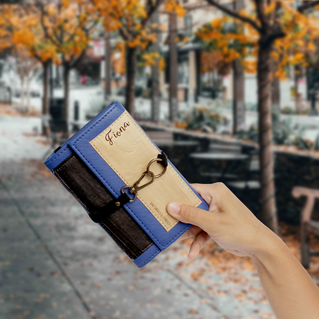 A vegan leather compact journal and passport holder with a vegan leather top flap, blue leather border, black leather body, and a laser engraved name "Fiona" on the top right corner.