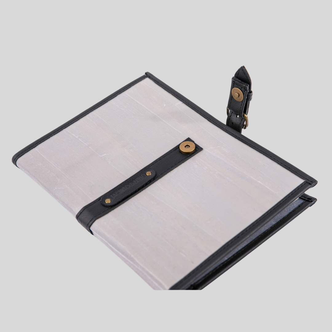 A light gray vegan leather notebook laying on a surface with its black leather closure strap opened.