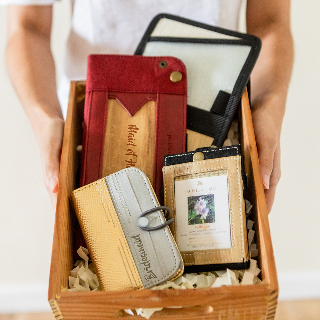 A gift box for Bridesmaids that contains a card and picture holder in a gold and gray color with "Bridesmaids" engraved on it, a black ID lanyard, a red foldable vegan leather tray, and other vegan leather items.