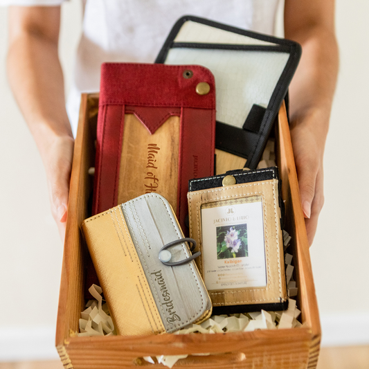 A gift box for Bridesmaids that contains a card and picture holder in a gold and gray color with "Bridesmaids" engraved on it, a black ID lanyard, a red foldable vegan leather tray, and other vegan leather items.