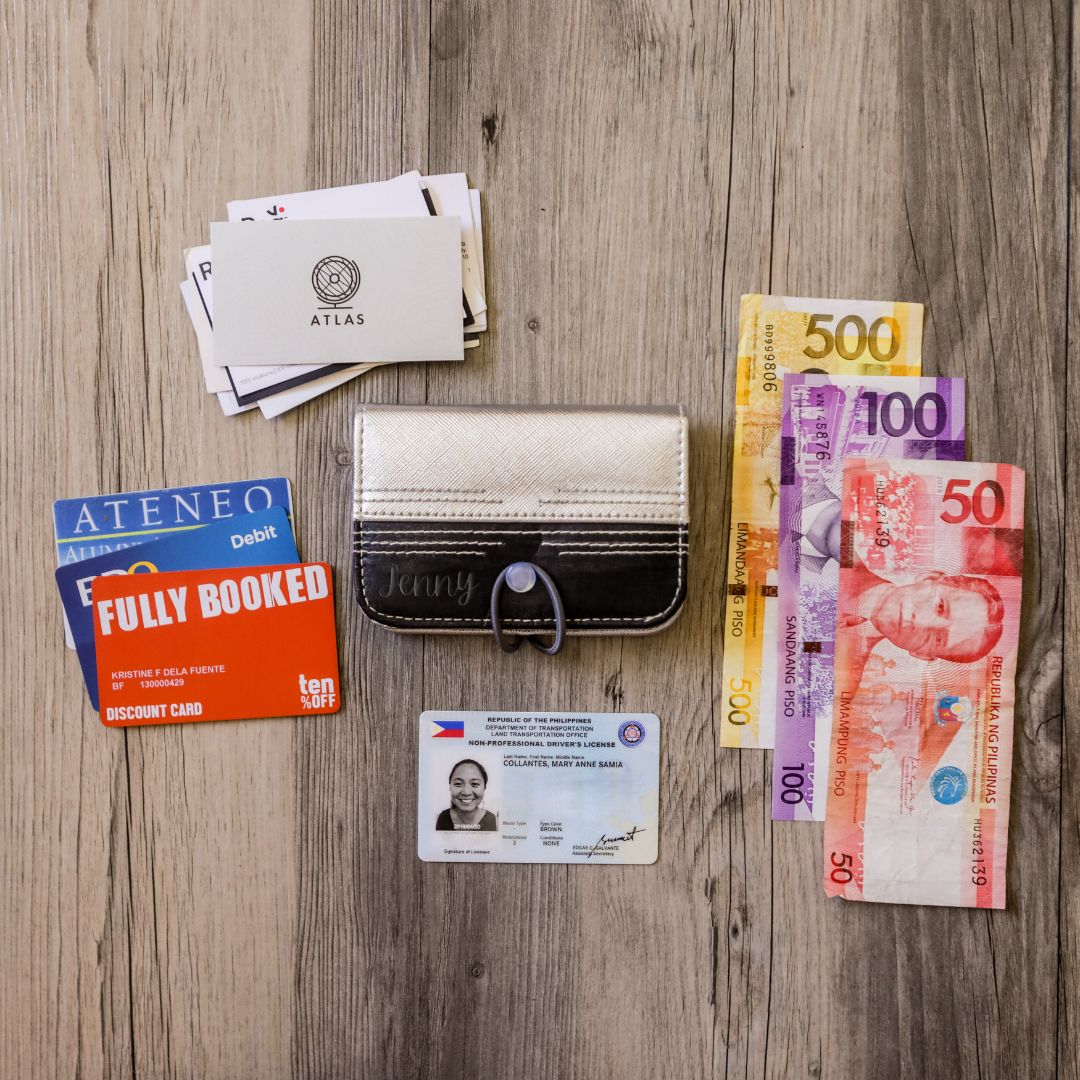 A silver and black vegan leather card wallet surrounded by money bills and credit cards