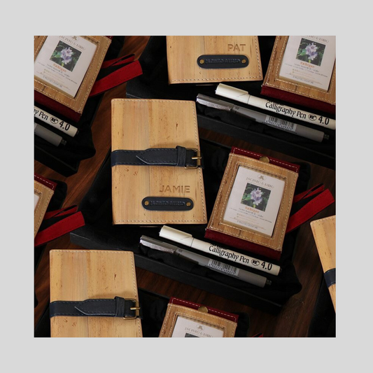 A gift box containing a vegan leather journal with a personal name engravement, along with a vegan leather ID lanyard and some calligraphy pens.
