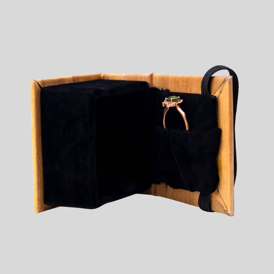 A side view shot of a vegan leather jewelry box laying horizontally on its side, slightly ajar, with an emerald and gold ring tucked in the compartment inside the box.
