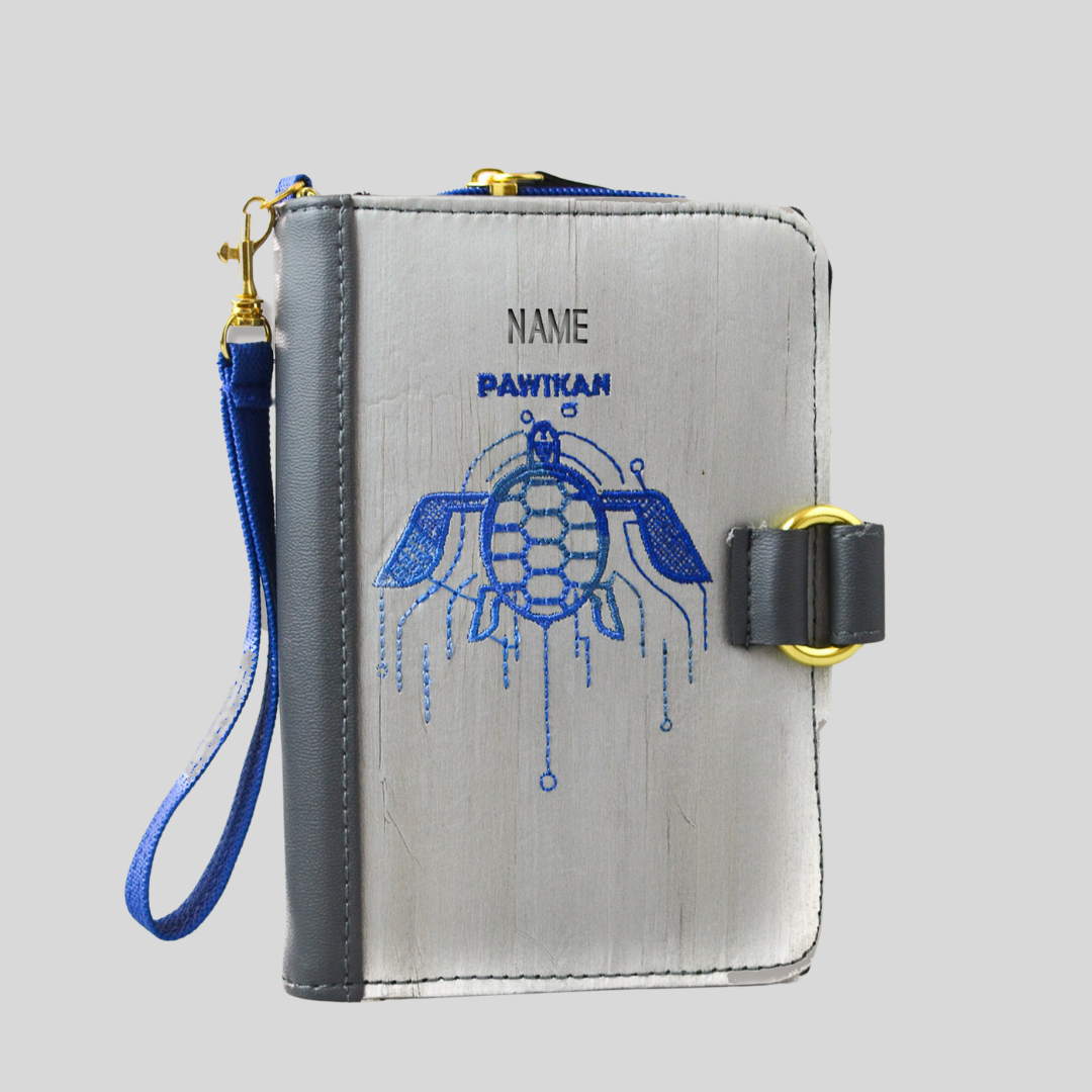 A light gray vegan leather journal that has a blue embroidered turtle on its cover.