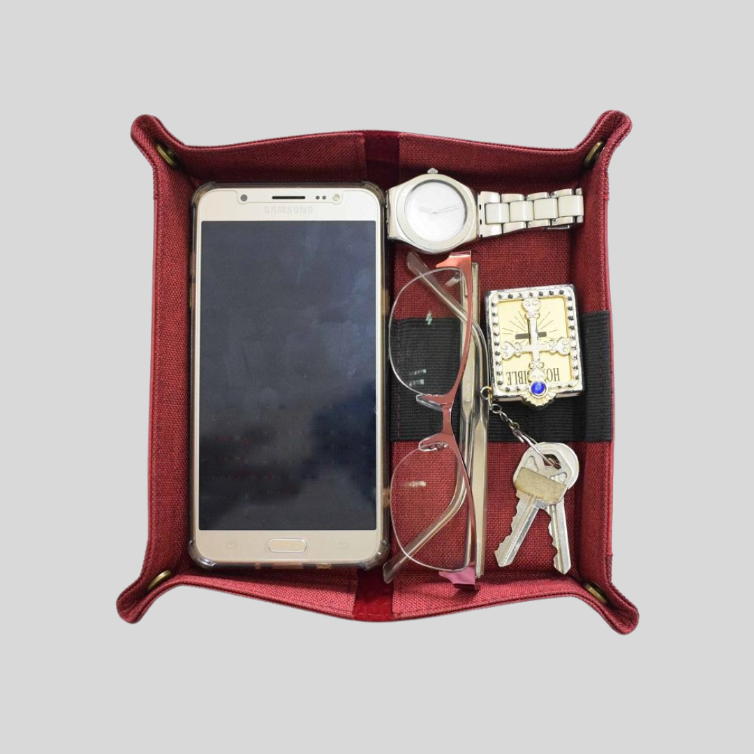 A red vegan leather bed-side tray storing a pair of glasses, an iPhone, car keys, and a watch neatly.