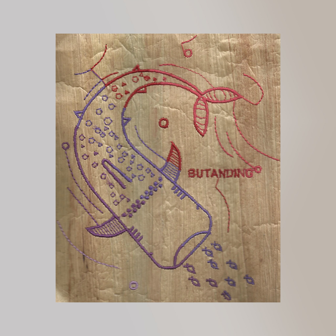 A dual-colored embroidered illustration of a 'Butanding' or whale shark on a piece of water hyacinth vegan leather with a wood texture.