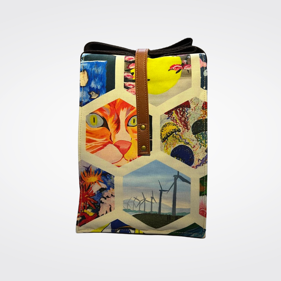 A uniquely designed tote bag featuring a collage of hexagonal art panels, including a prominent orange tabby cat face with bright green eyes, alongside scenes of wind turbines, colorful floral abstractions, and aquatic-themed artwork, finished with brown vegan leather straps.
