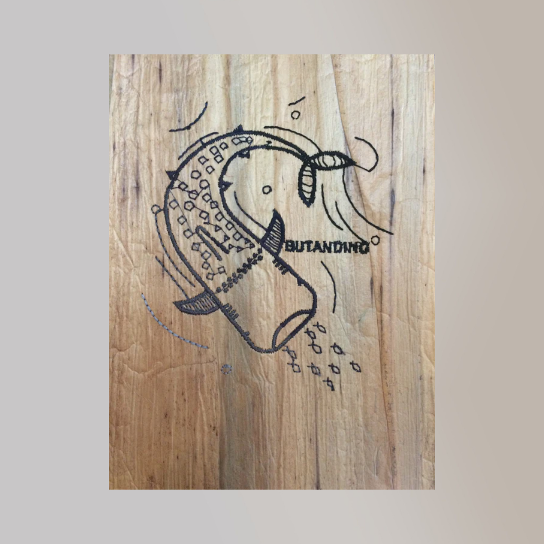 An embroidered illustration of a 'Butanding' or whale shark on a piece of water hyacinth vegan leather with a wood texture.