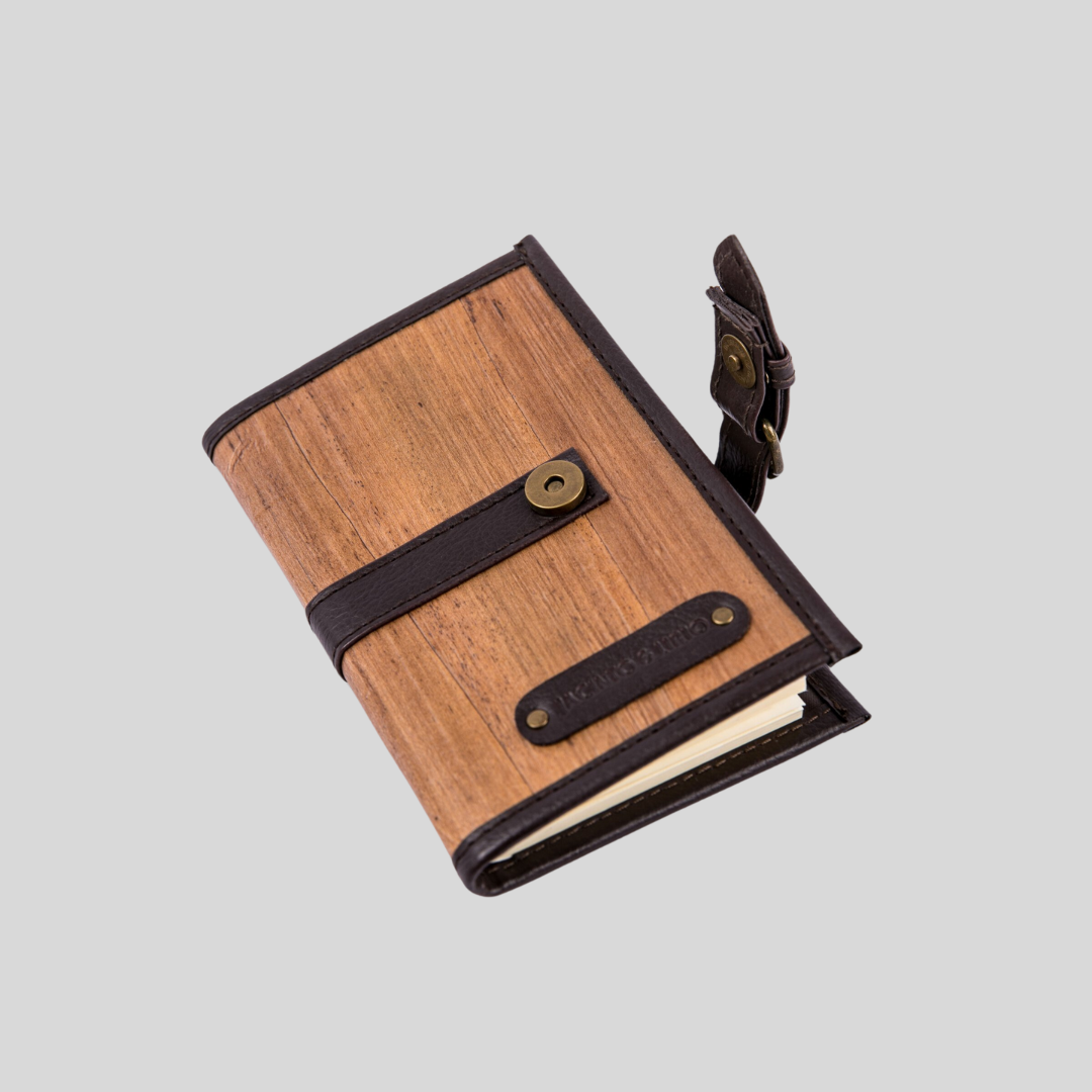An opened notebook with its cover made of vegan leather and dark brown hemming all around the sides, top, and bottom.