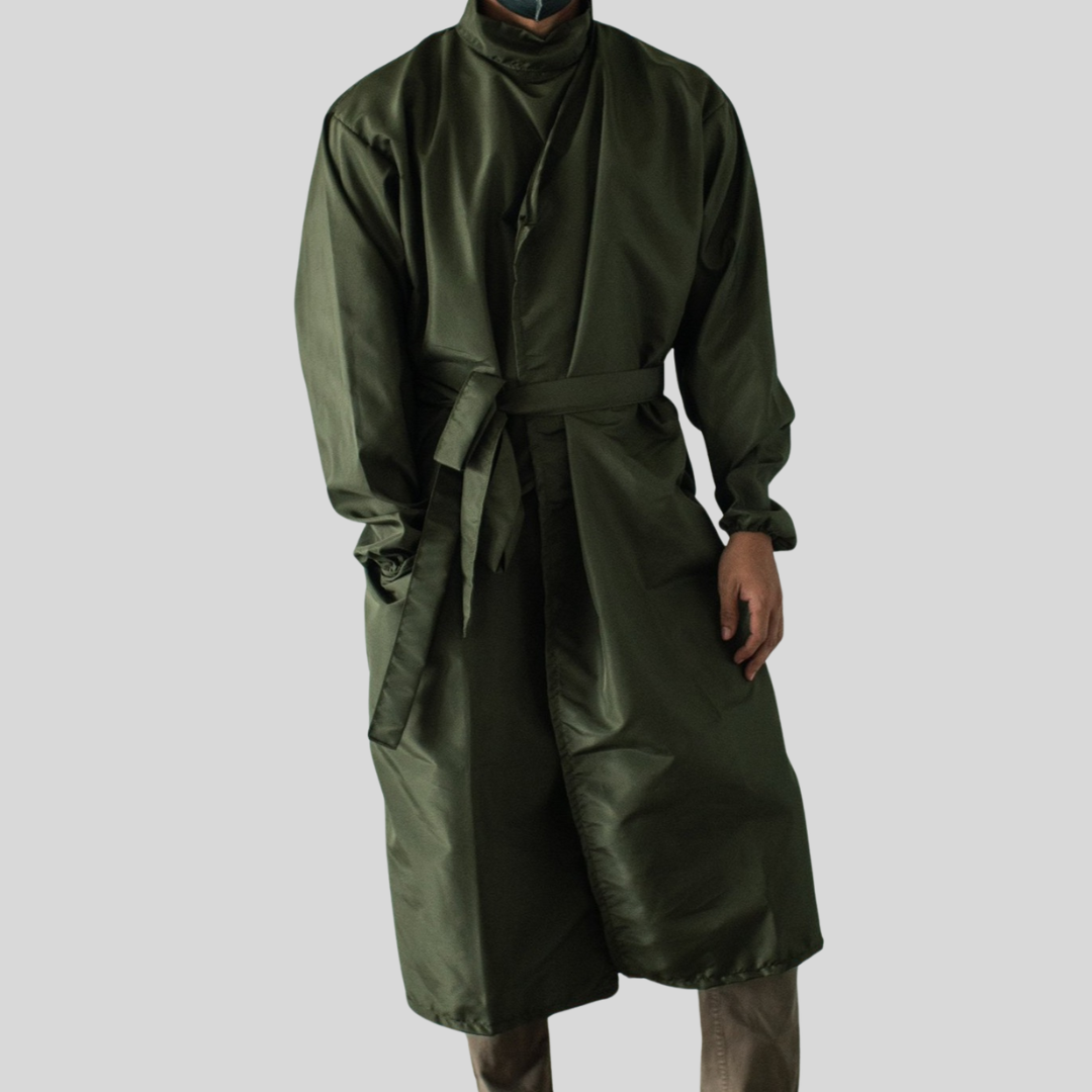 A man wearing a mask and a forest green microfiber PPE suit that is fully closed by buttons and a built-in belt knotted to the side.