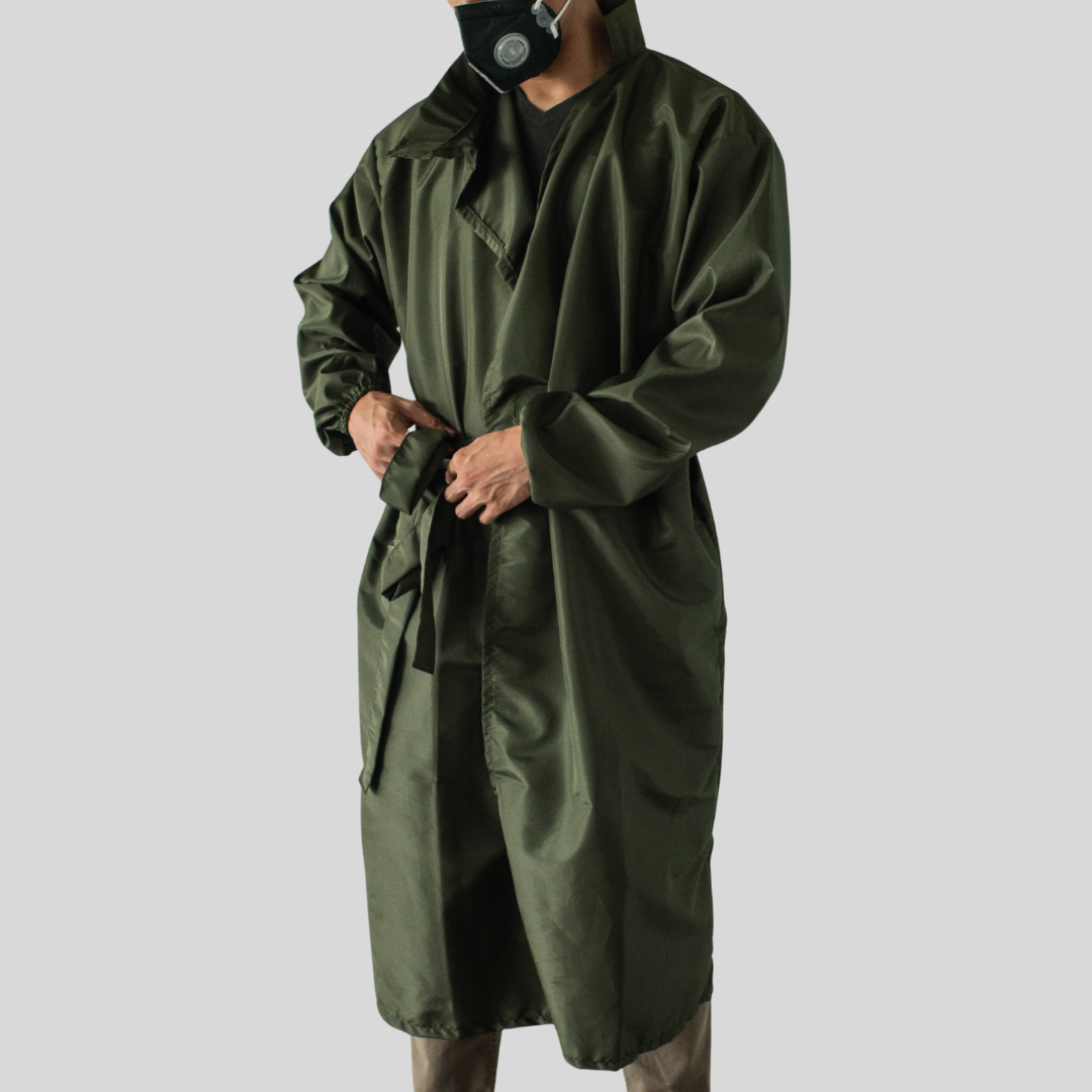 A man wearing a black surgical mask and a dark green water-proof PPE suit, knotting the suit closed by its thin built-in belt.