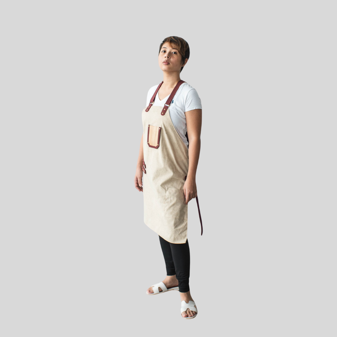 A woman standing and posing while wearing a cream-colored apron that reaches her knee.