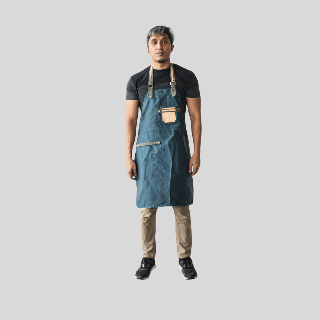 A man standing and wearing a dark blue apron that reaches knee-length.