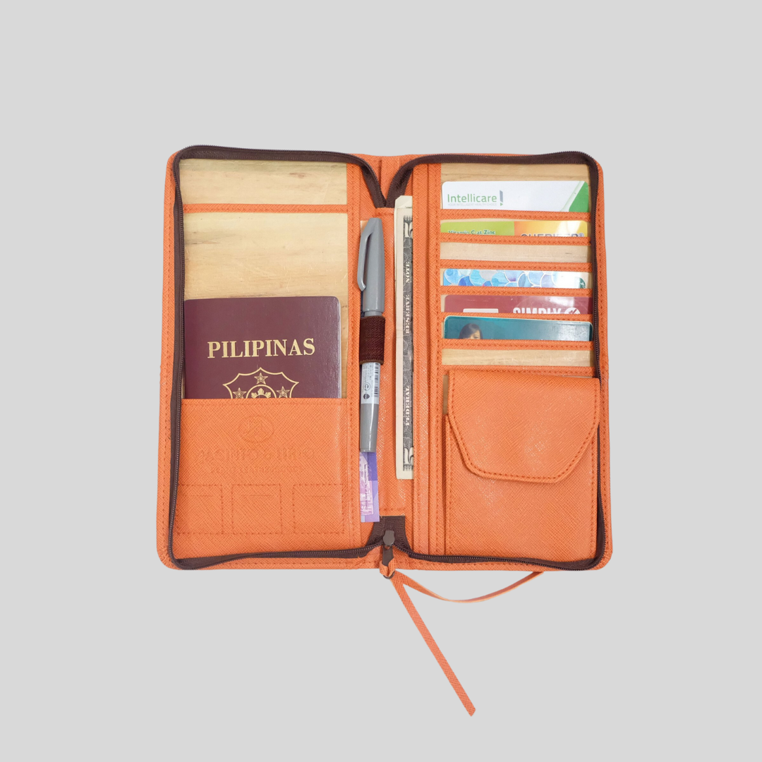 An orange vegan leather travel purse opened to show its many features such as a passport pocket, pen holder, wallet, card holders and coin purses all separated for easy access.