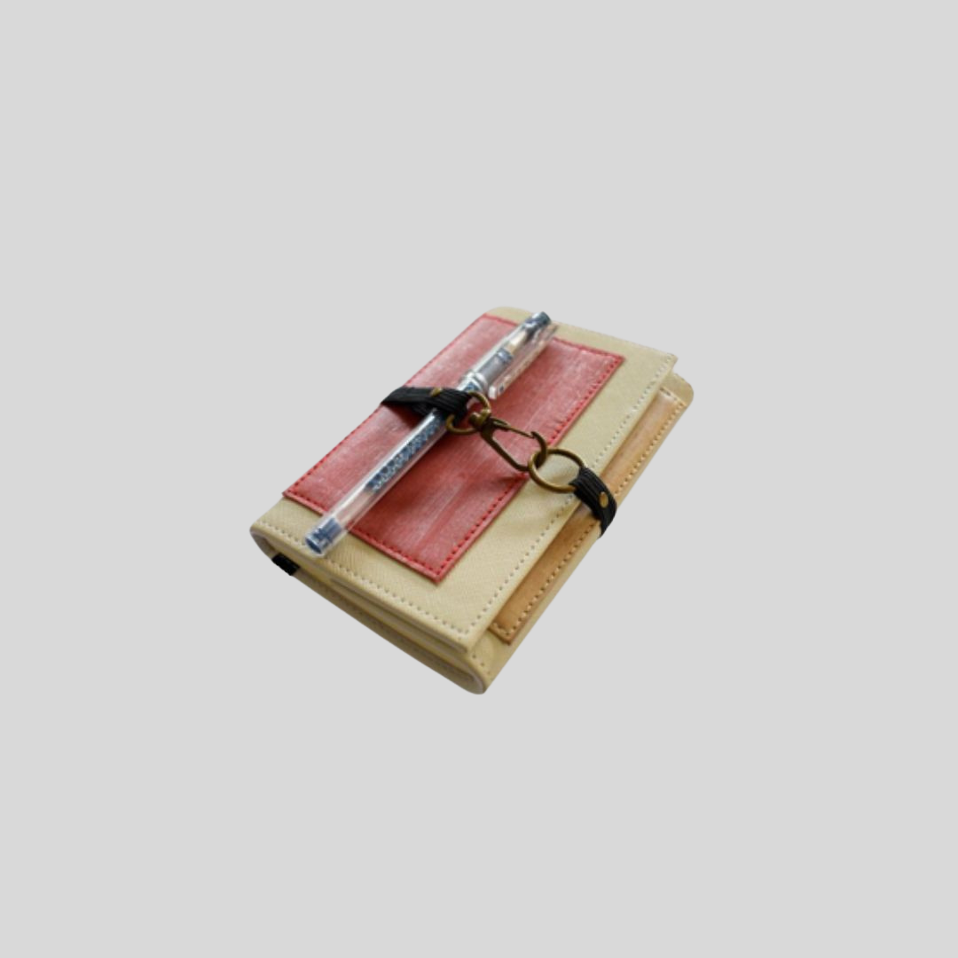 A vegan leather mini notebook accessory holding a pen by its black garter and metal hook closure wrapped around the outside.