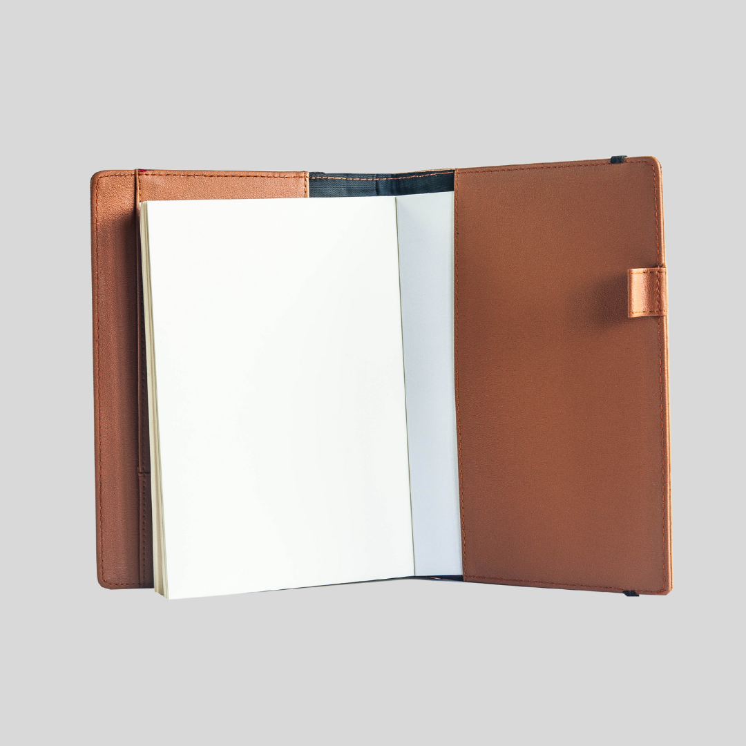 Brown leather notebook with blank white pages, laying opened in front of a plain gray background.