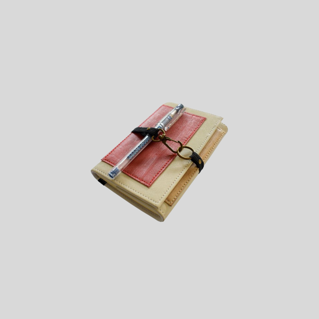 A vegan leather wallet holds a pen in between its garter metal hook closure.