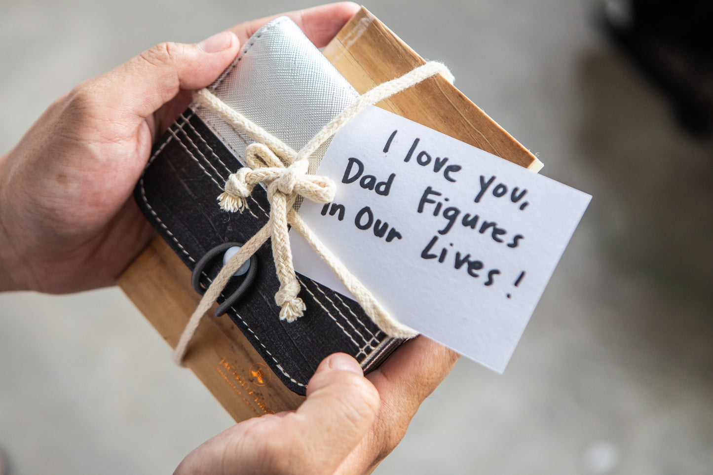 A vegan leather card wallet and mini notebook that is tied together by a string, along with a piece of paper with the message "I love you Dad Figures in our lives!" on it.