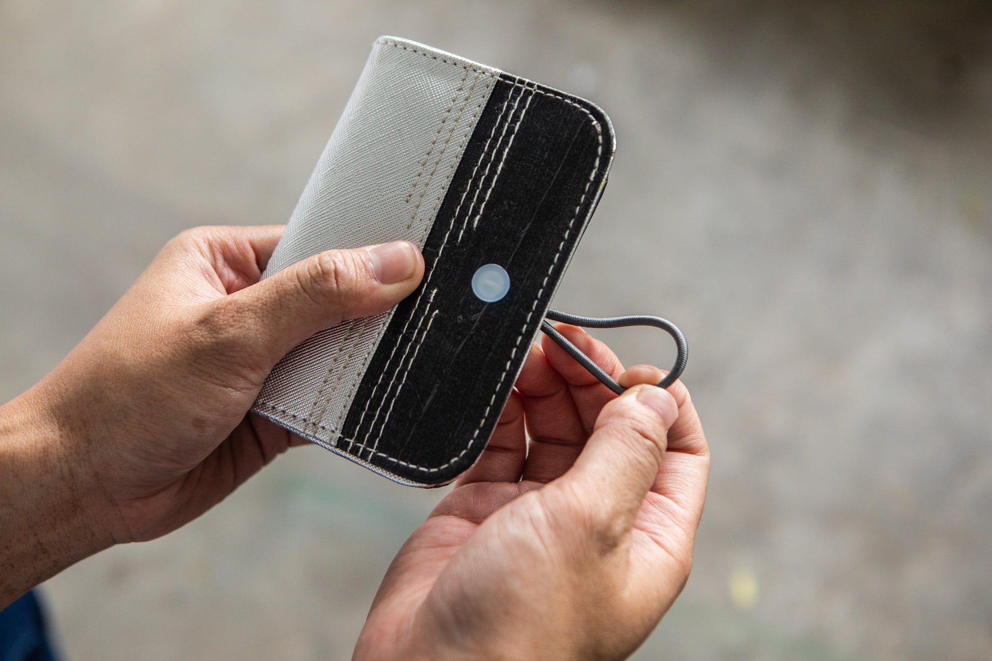 A pair of hands carefully opens a mini vegan leather card wallet that is gray and black in color.