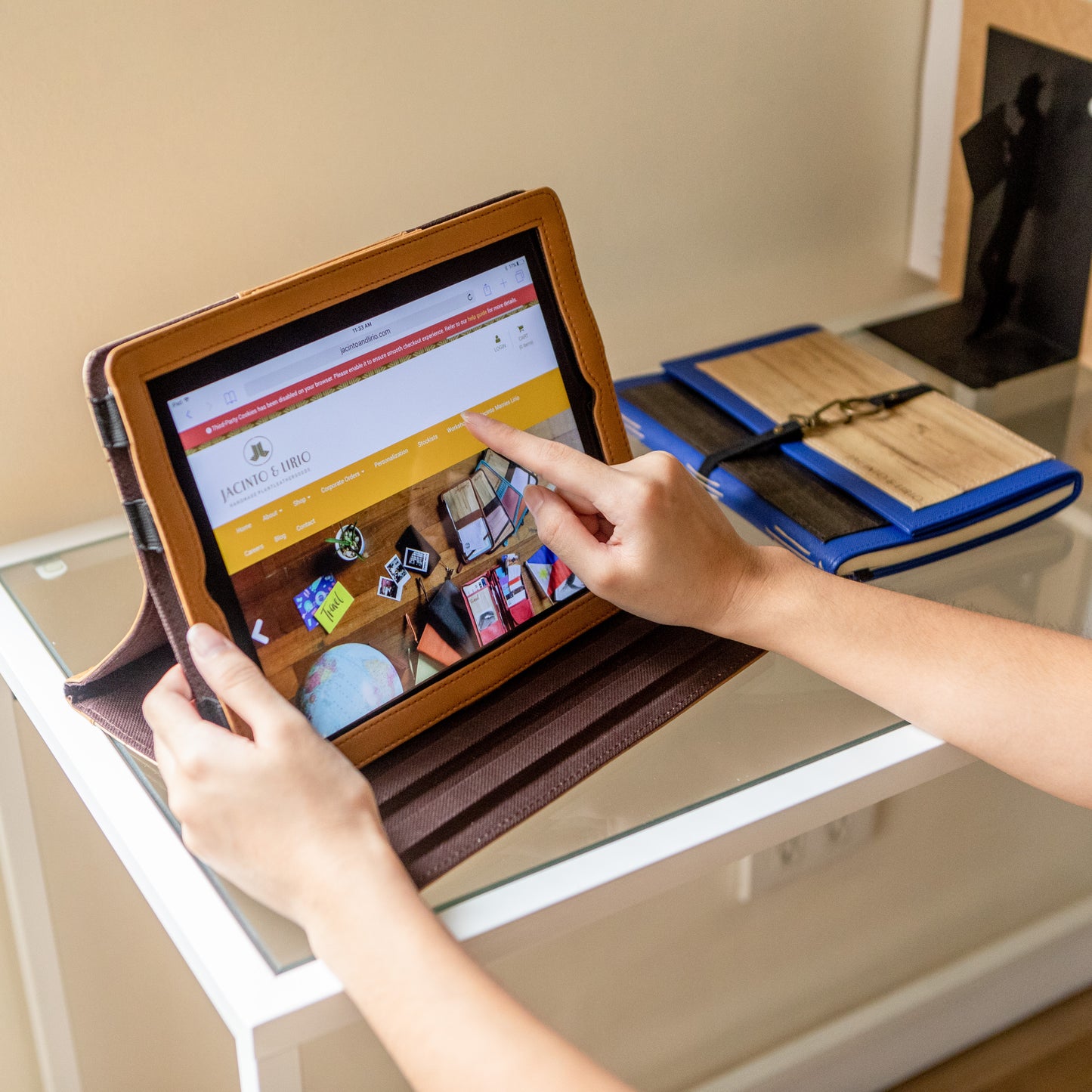 Ipad opened to the Jacinto & Lirio online store, encased in a brown Vegan Leather sustainable ipad case with a journal to the right of it.