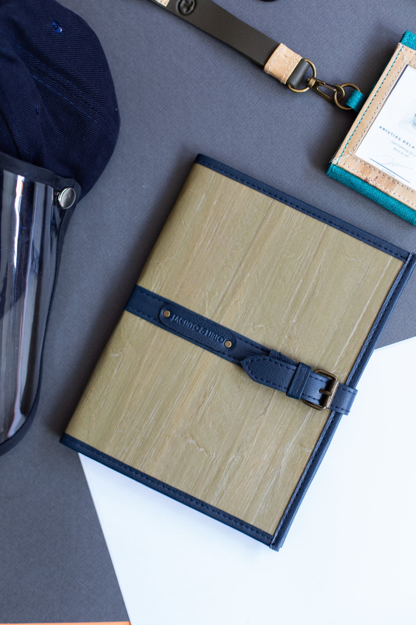 A vegan leather notebook with a gray cover, that also has blue leather hemming and belt buckle closure.
