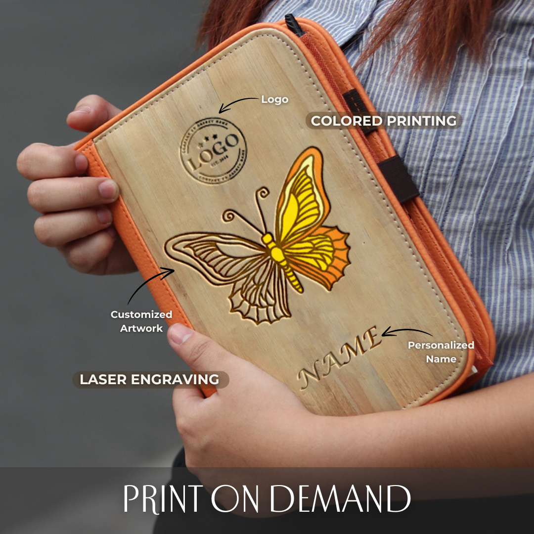A woman holding an orange and wood-colored vegan leather A5 planner that has colored laser engraving of a butterfly on it, with an engraved logo on top and a personalized name on the bottom.