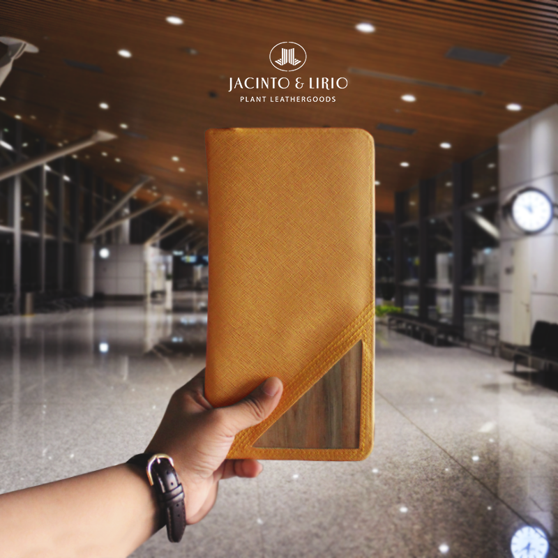 An orange vegan leather wallet being help up in front of an empty airport.