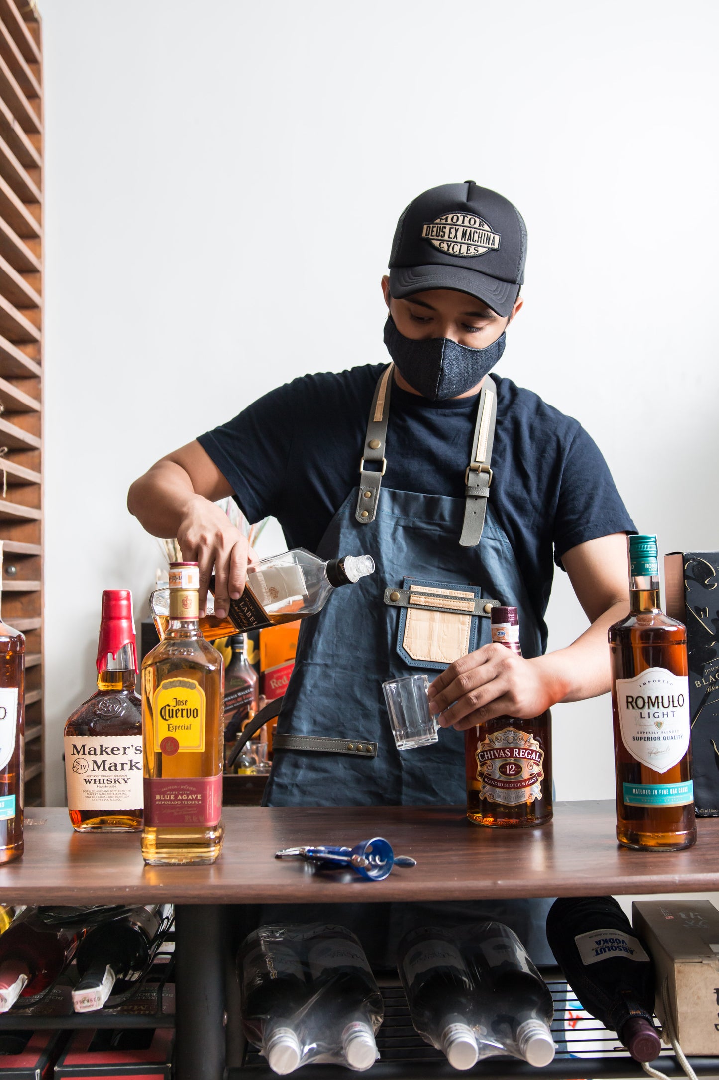 A barista making an alcohol drink while wearing a dark brown apron that has a rustic aesthetic.