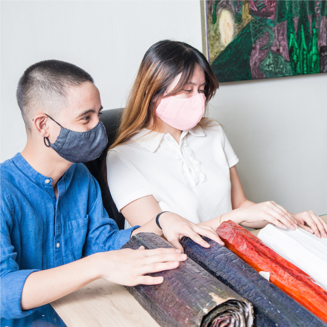 Two people wearing masks, picking out wallpaper from various designs and colors.