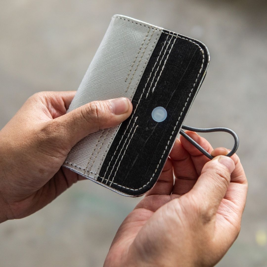 A person opening a dual-colored card wallet with a garter closure.