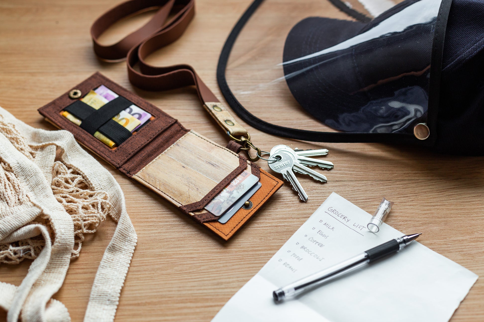 A brown ID lanyard made of vegan leather with built-in card compartments and a bill pocket, laying haphazardly on a desktop surface.