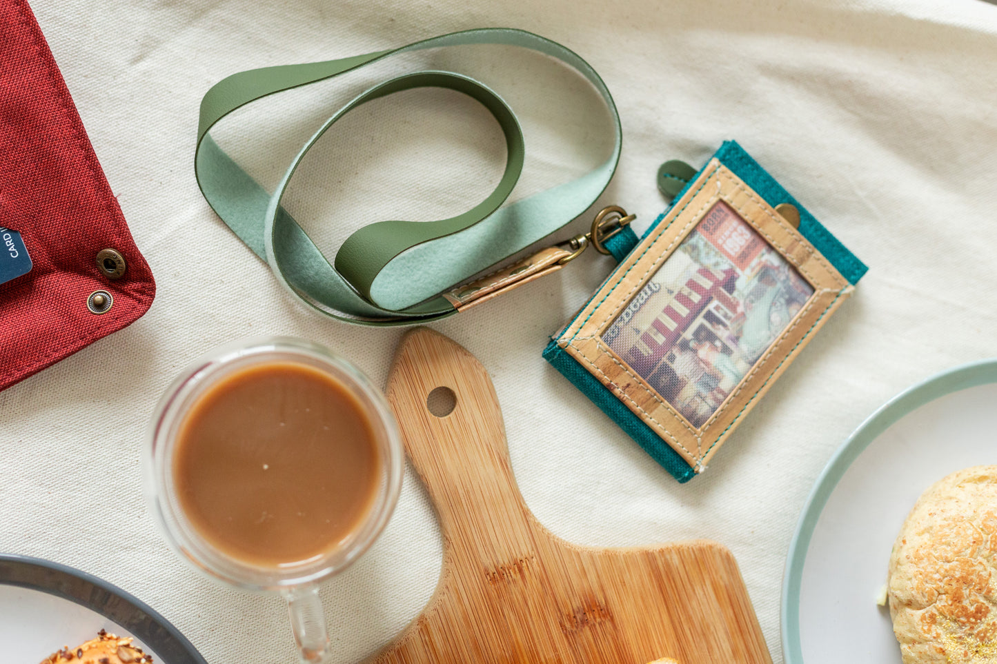 A teal-colored vegan leather lanyard next to a chopping board and a cup of coffee.