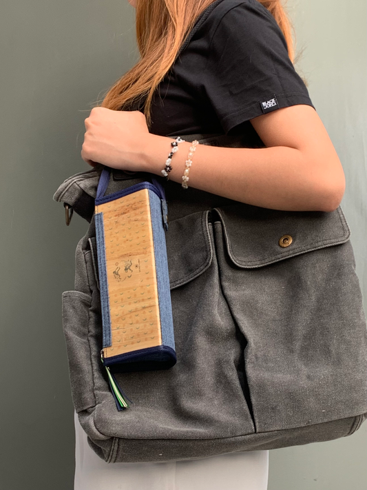 A woman in a black shirt holding up a big gray bag that has an expandable vegan leather rectangular pencil case with denim blue accents, attached to the strap of the bag.