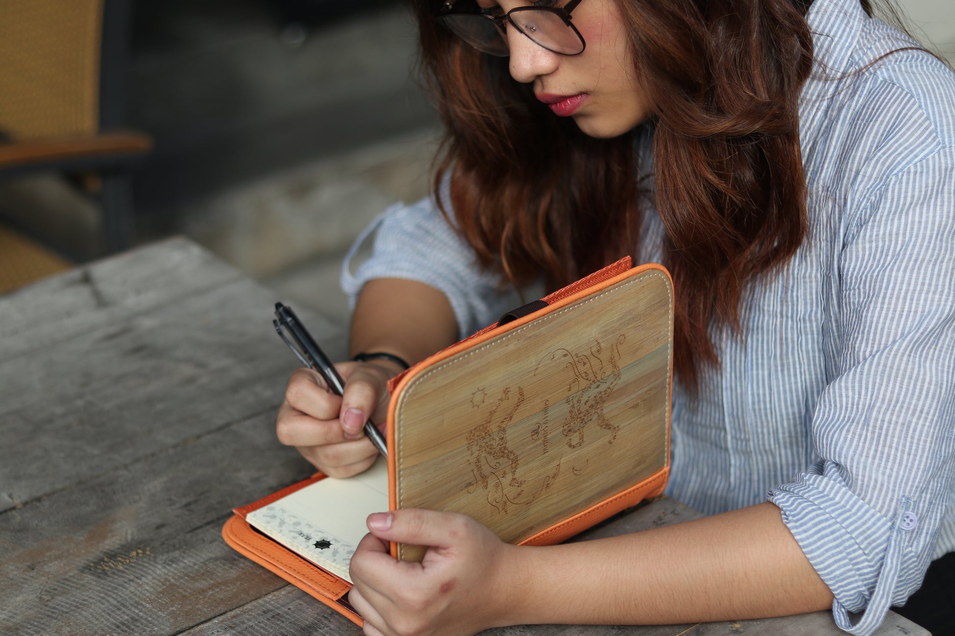 A woman writing in a orange vegan leather notebook.
