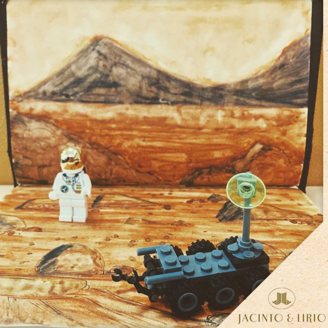 A lego set up of an astronaut and a mars rover in front of a drawn backdrop of mars.