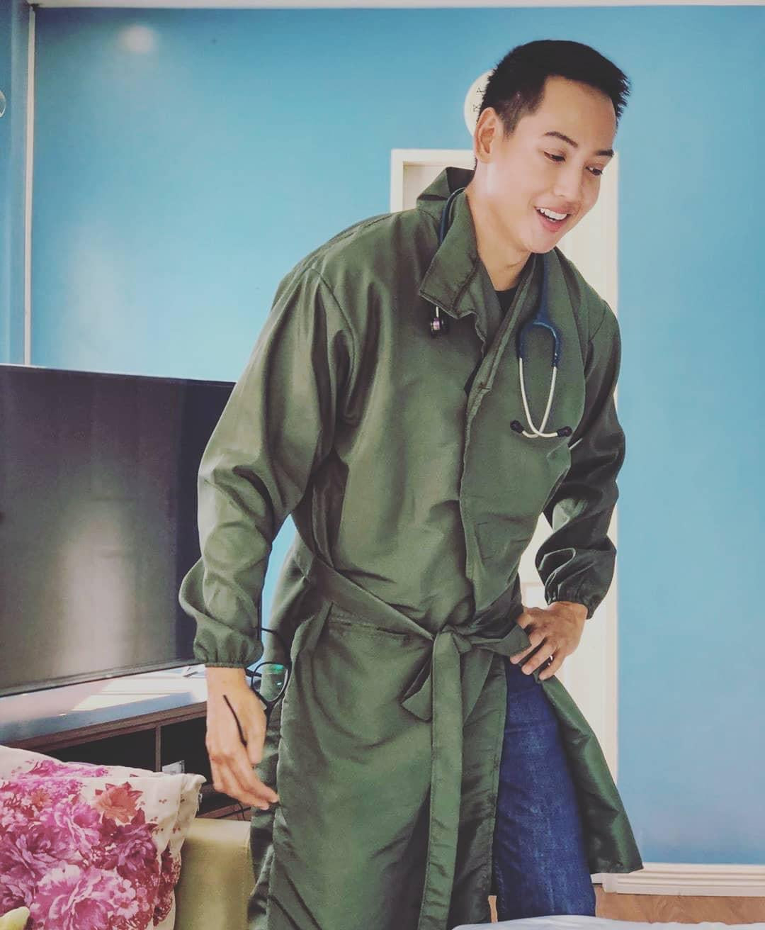 A doctor wearing an army green kimono style PPE suit with the ribbon belt knotted around his waist.