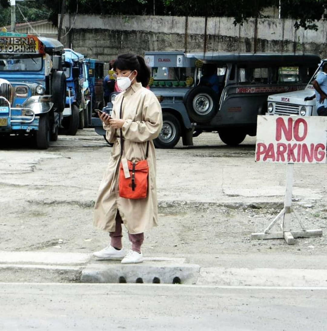 A woman wearing a stylish beige microfiber PPE suit that looks like a trench coat, amongst a background of jeeps.