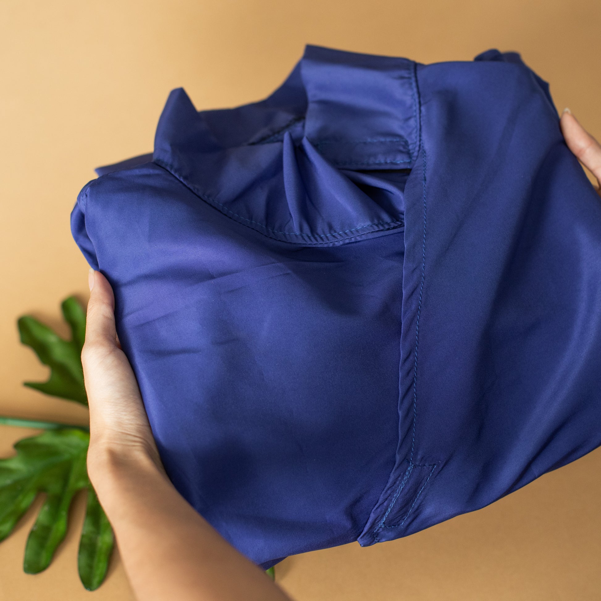 A folded up blue microfiber and water-resistant PPE suit held up by a pair of hands.