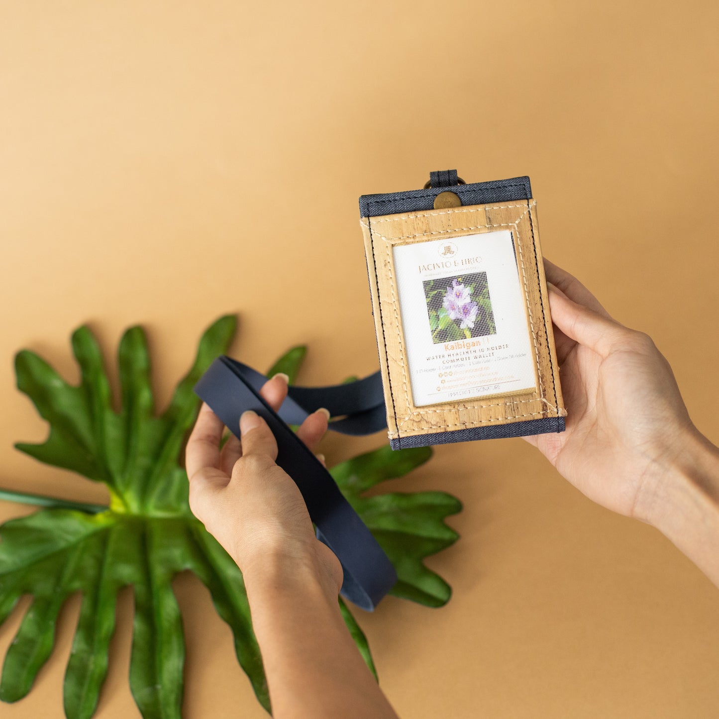 A navy blue vegan leather ID lanyard being held up in front of a beige background.