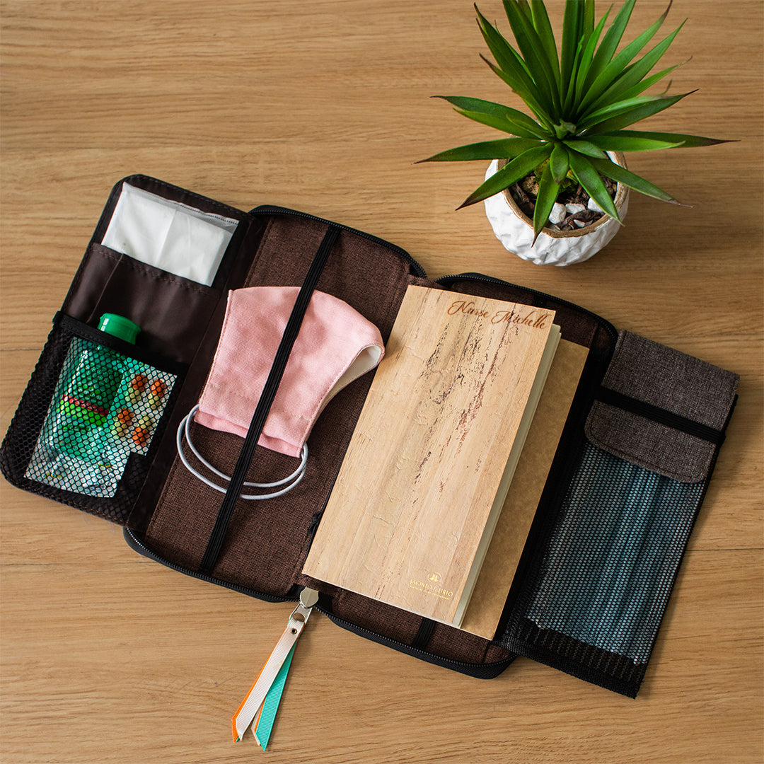 A vegan leather planner that comes in a zipped wallet form is laid on a table next to a plant.