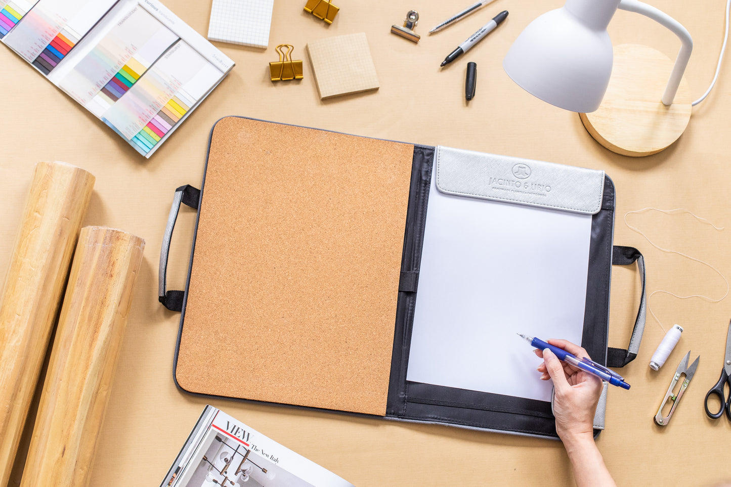 A working desktop with a corkboard planner and rolls of vegan leather wallpaper.