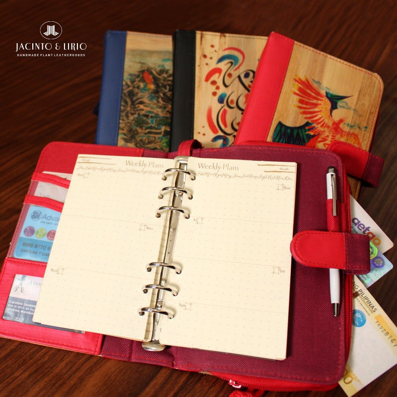 Refillable notebooks made of vegan leather in different colors with custom drawings on their covers laid on a wooden surface.