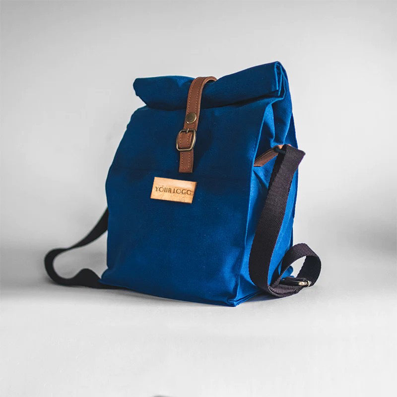 A dimetric view of an ocean blue lunch bag with a vegan leather name patch in front and a water-repellant exterior.