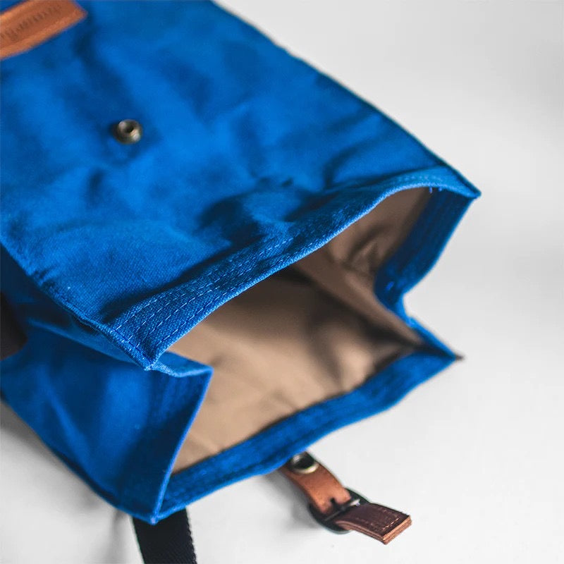 An open blue lunch bag, showing an un-closed clasp and a polyester taffeta inside lining, with a waxed canvas exterior.