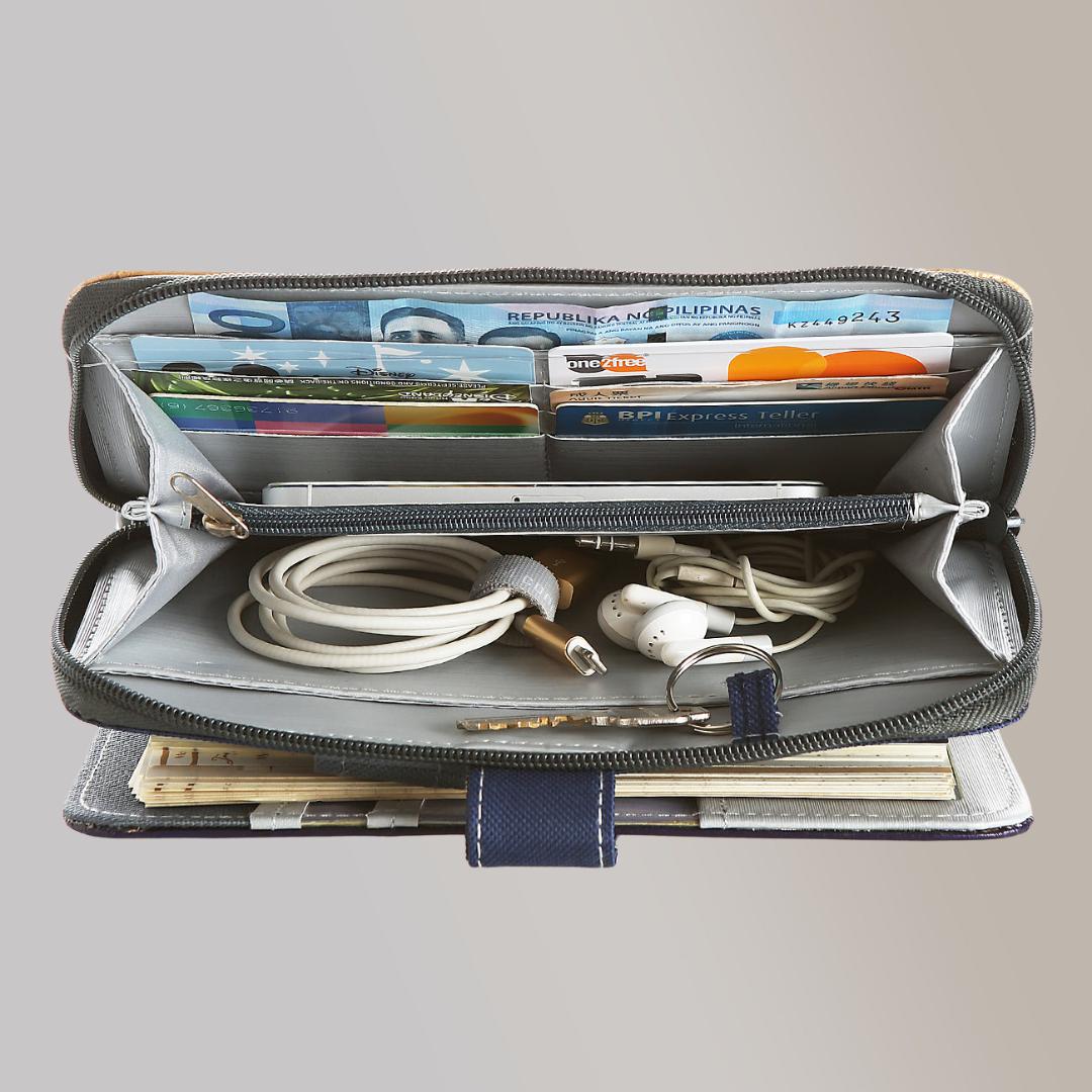A top view of the opened wallet attached to a gray leather notebook, which contains wired earphones, cords, bills, a phone, and cards.