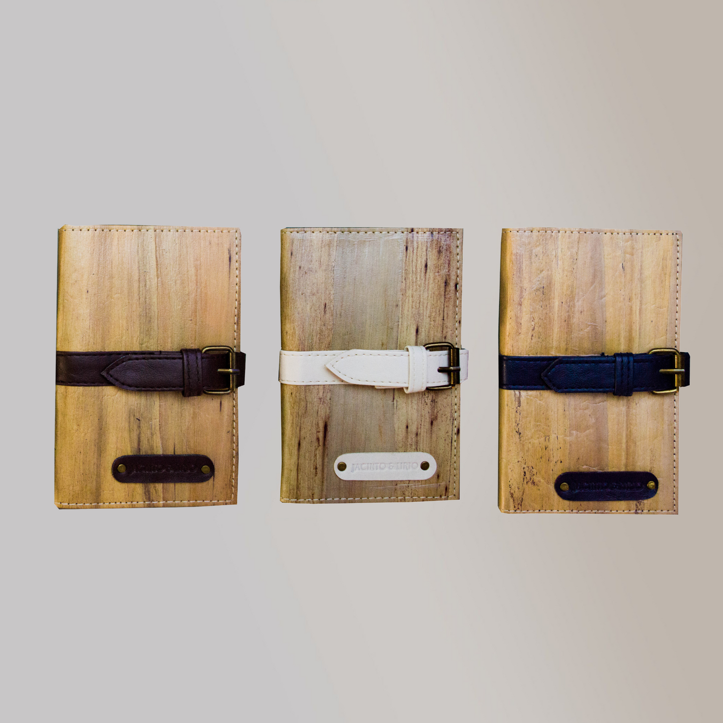 Three vegan leather journals lined up side by side with thick belt buckle closures in varying colors. One in a black color, one in white, and the last ina dark blue color.
