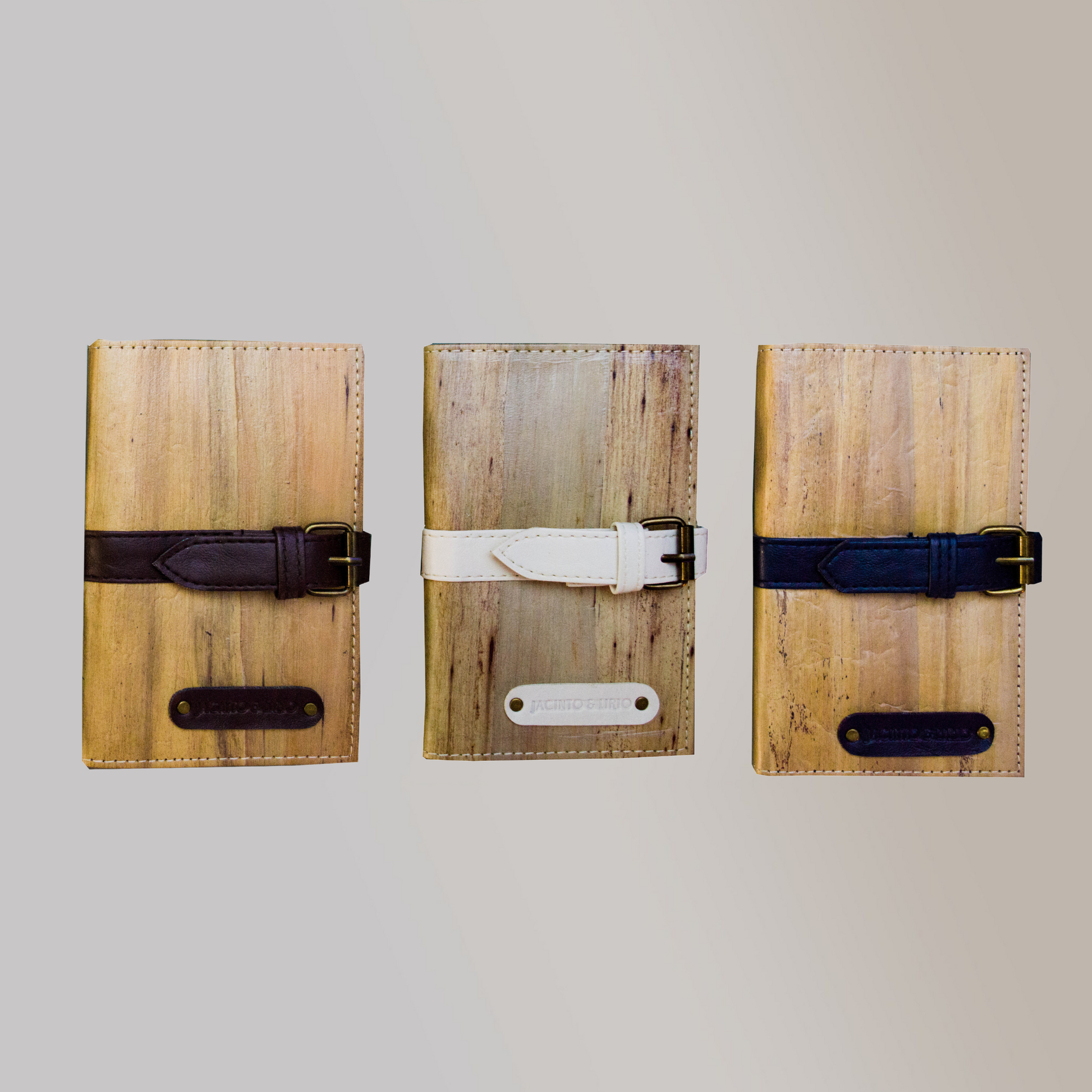 Three vegan leather journals lined up side by side with thick belt buckle closures in varying colors. One in a black color, one in white, and the last ina dark blue color.