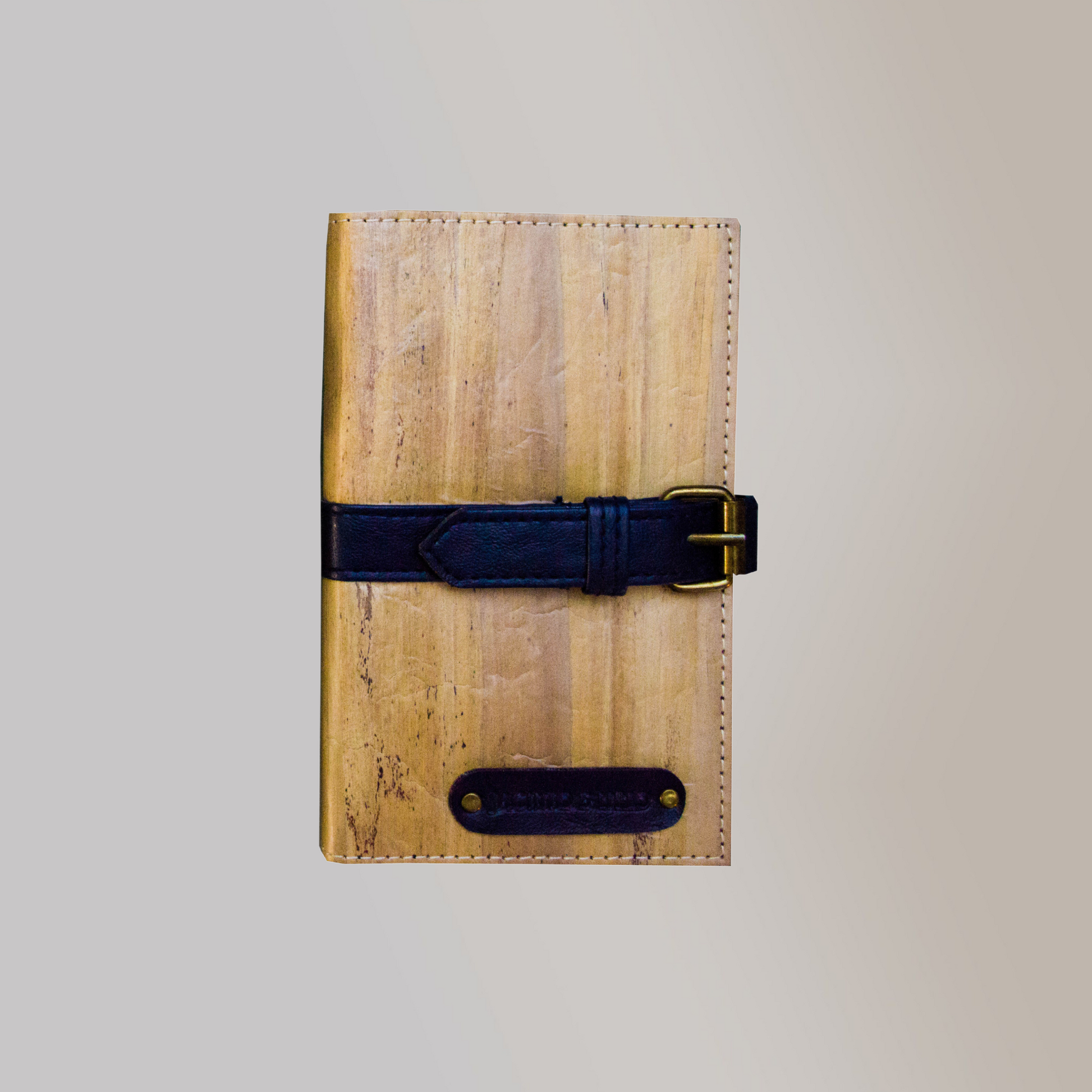 A vegan leather journal with a dark blue leather belt buckle closure.